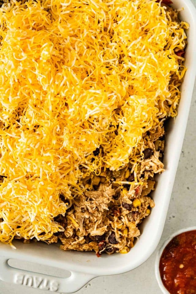 topping shredded chicken with cheese in a baking dish