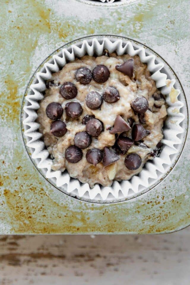 Muffin batter in a muffin tin topped with chocolate chips.