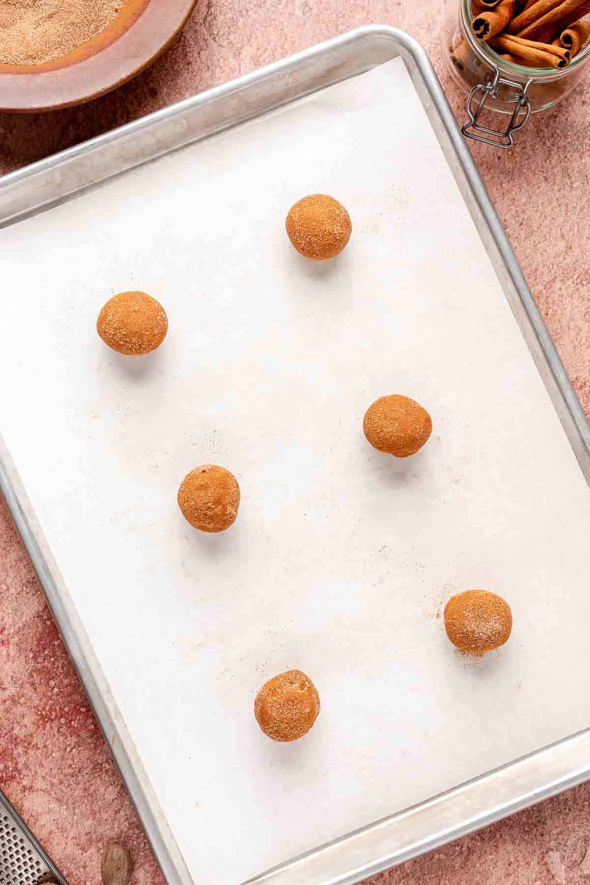 Rolled dough balls covered in cinnamon and sugar on a cookie sheet.