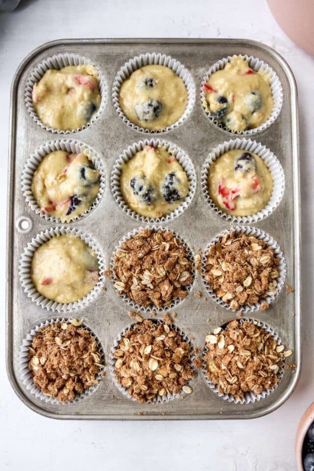 Streusel sprinkled over batter in a muffin tin.