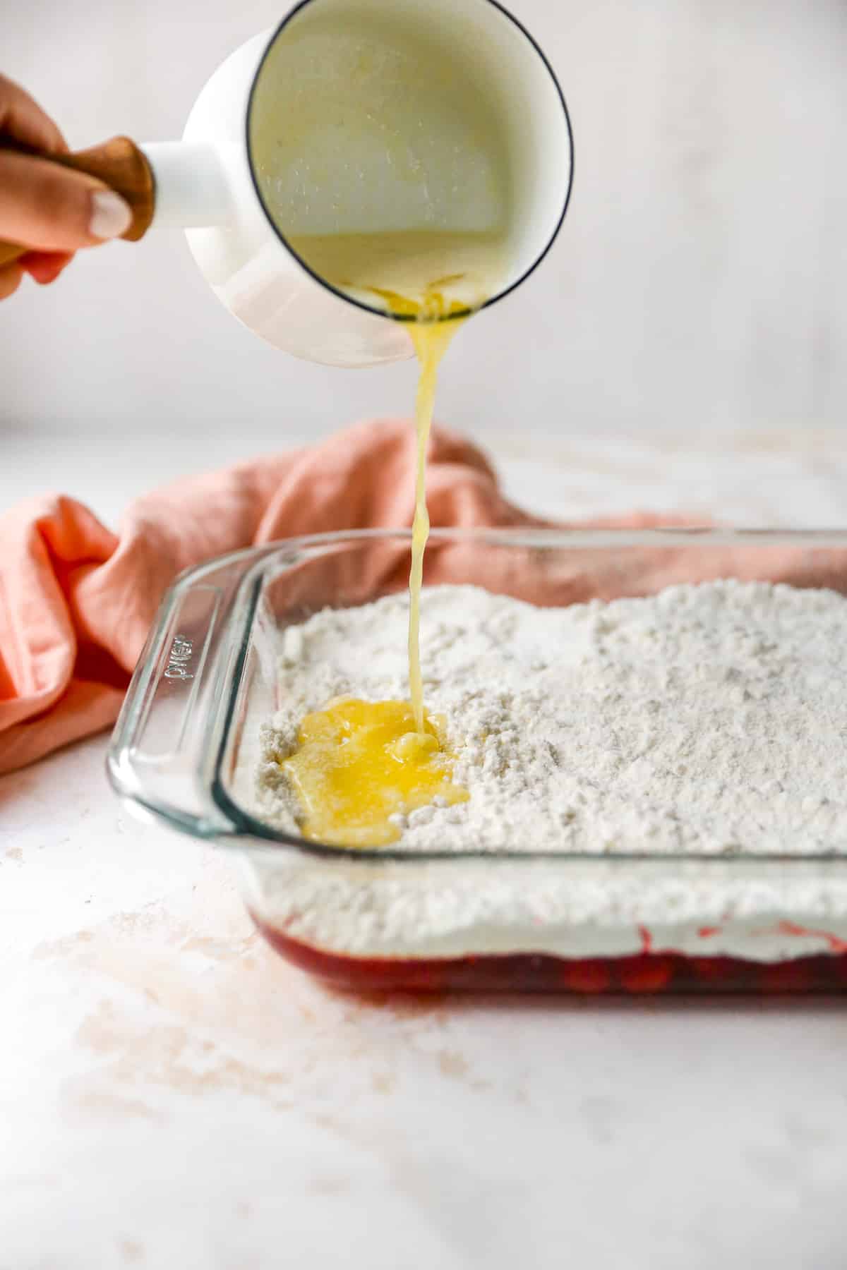 Pouring melted butter over cherry dump cake.