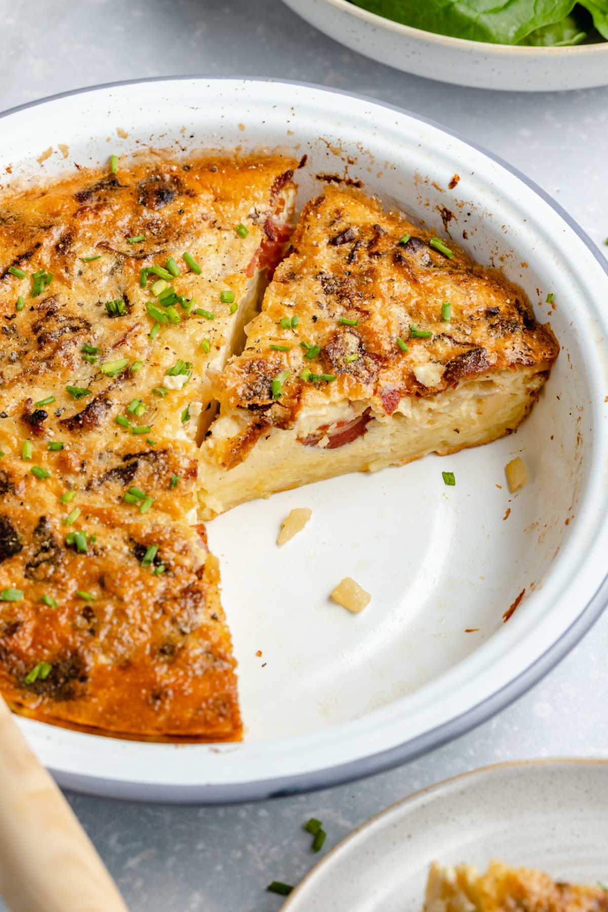 White pie dish with a bacon and Swiss quiche.