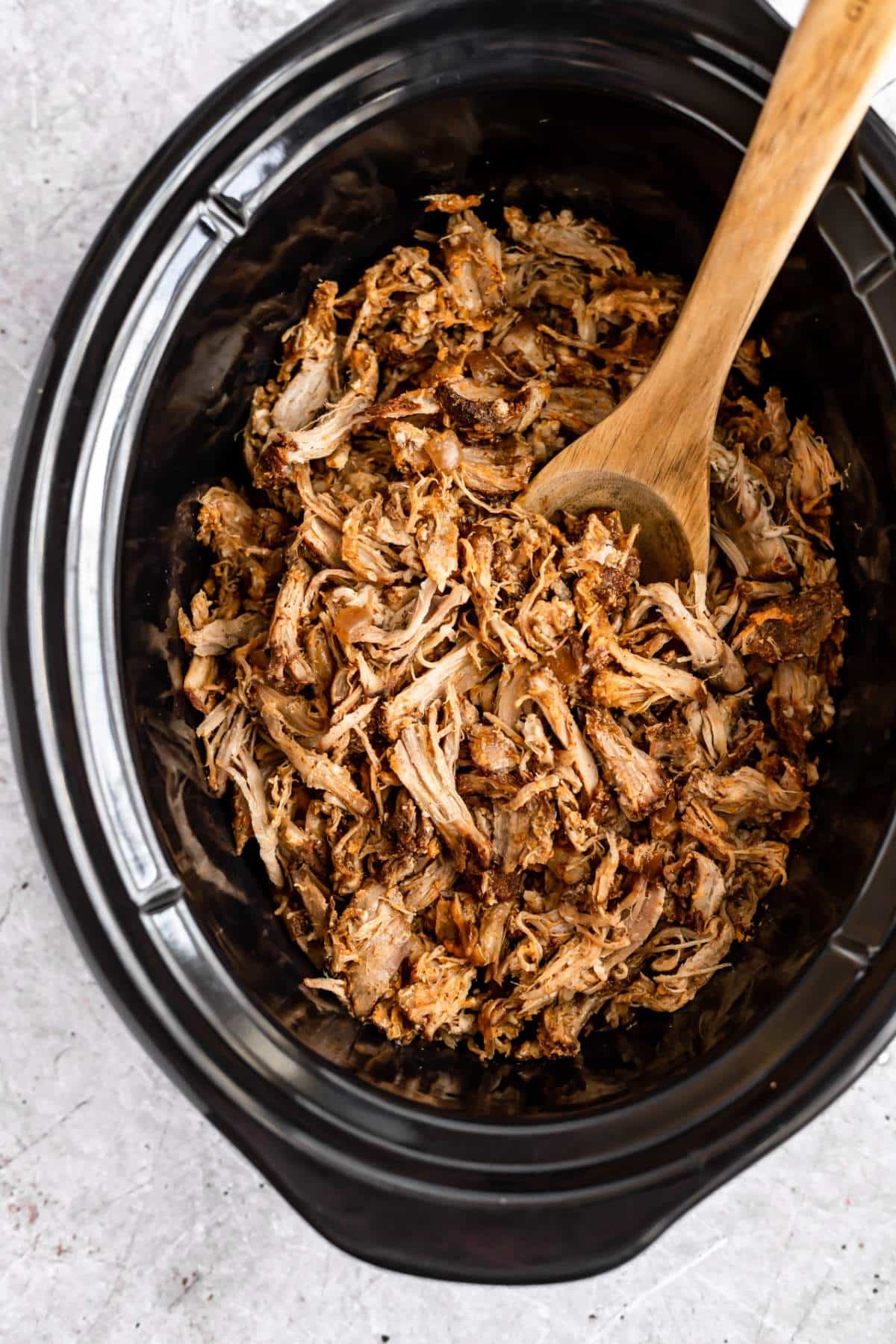 Shredded pulled pork in a slow cooker with a wooden spoon.