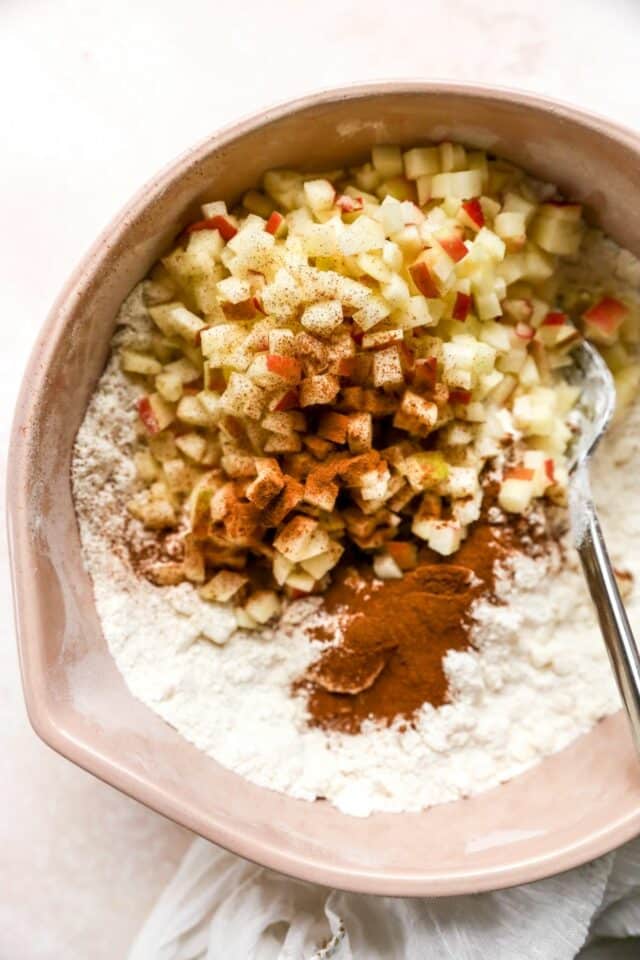 Adding diced apple and cinnamon to flour mixture in a large bowl.