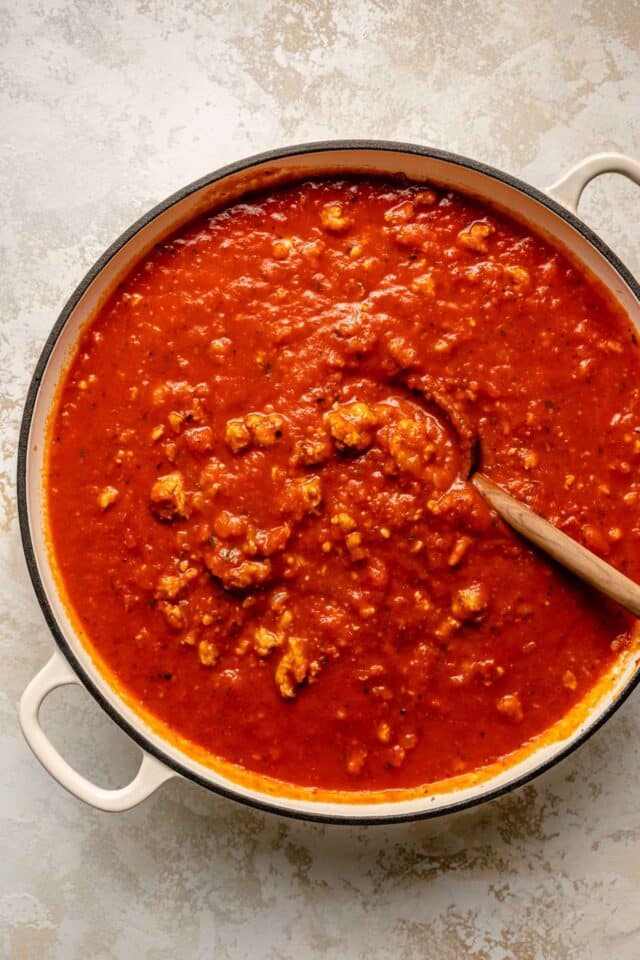 Stirring marinara into ground meat with a wooden spoon.