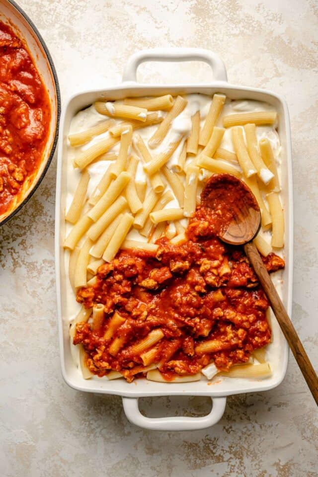 Assembling a pasta casserole with noodles and marinara.