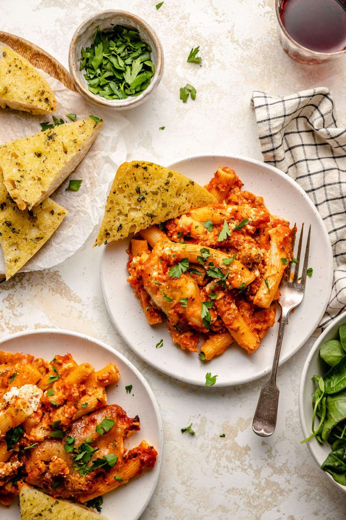 Servings of saucy pasta on white plates served with garlic bread.