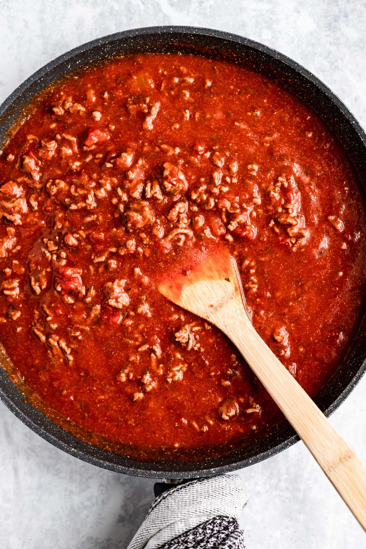 Stirring marinara sauce mixed with ground beef in a large skillet.