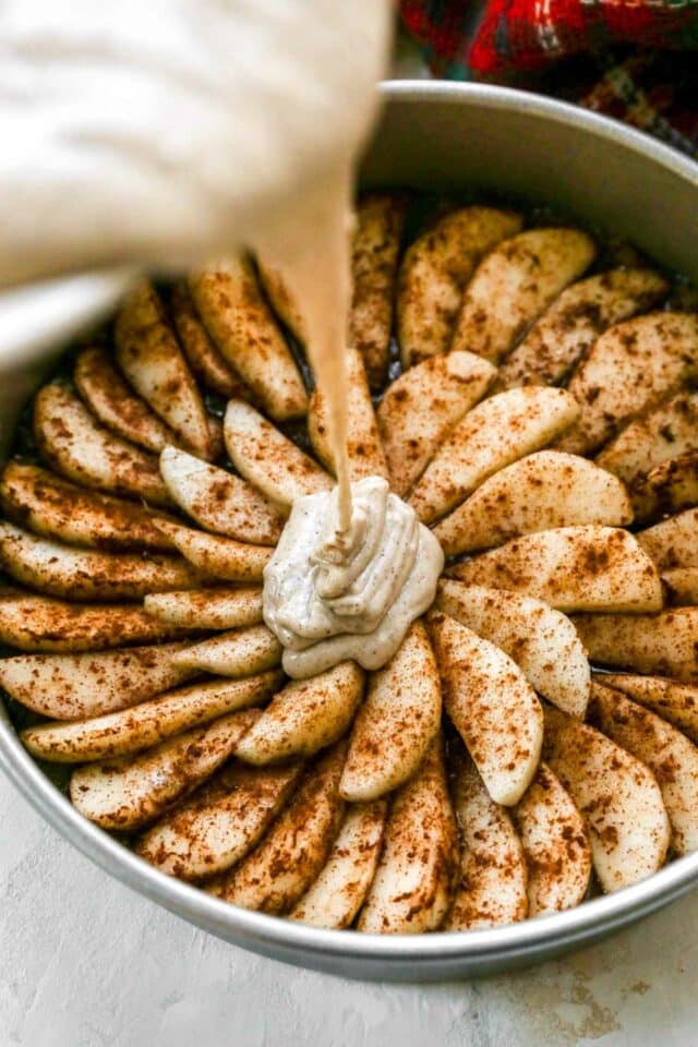 Pouring cake batter over pear slices in a cake pan.