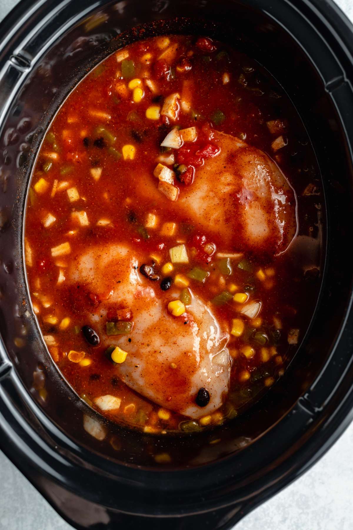 Chicken breasts, tomatoes, corn and black beans in a slow cooker.