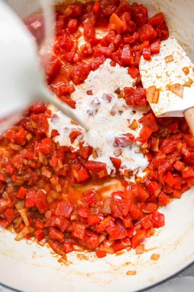 Adding cream to a pan with tomatoes and bell pepper cooking.