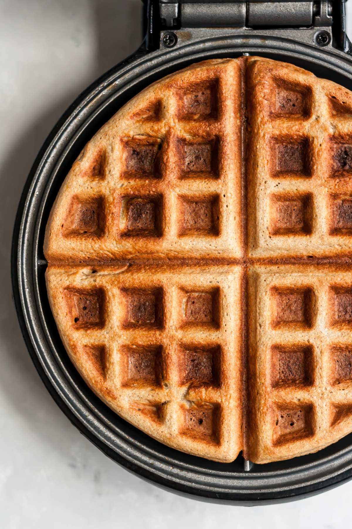 Banana oat waffles cooking on a waffle iron.