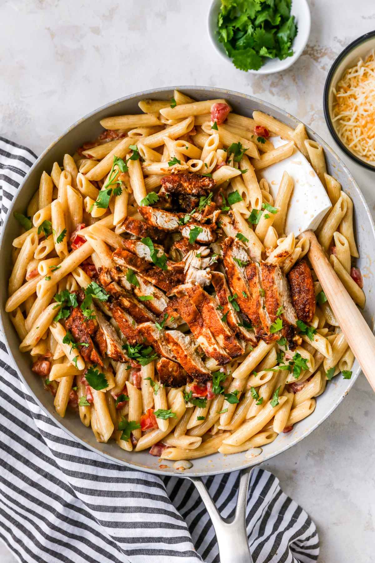 Sliced chicken atop penne pasta garnished with chopped cilantro.