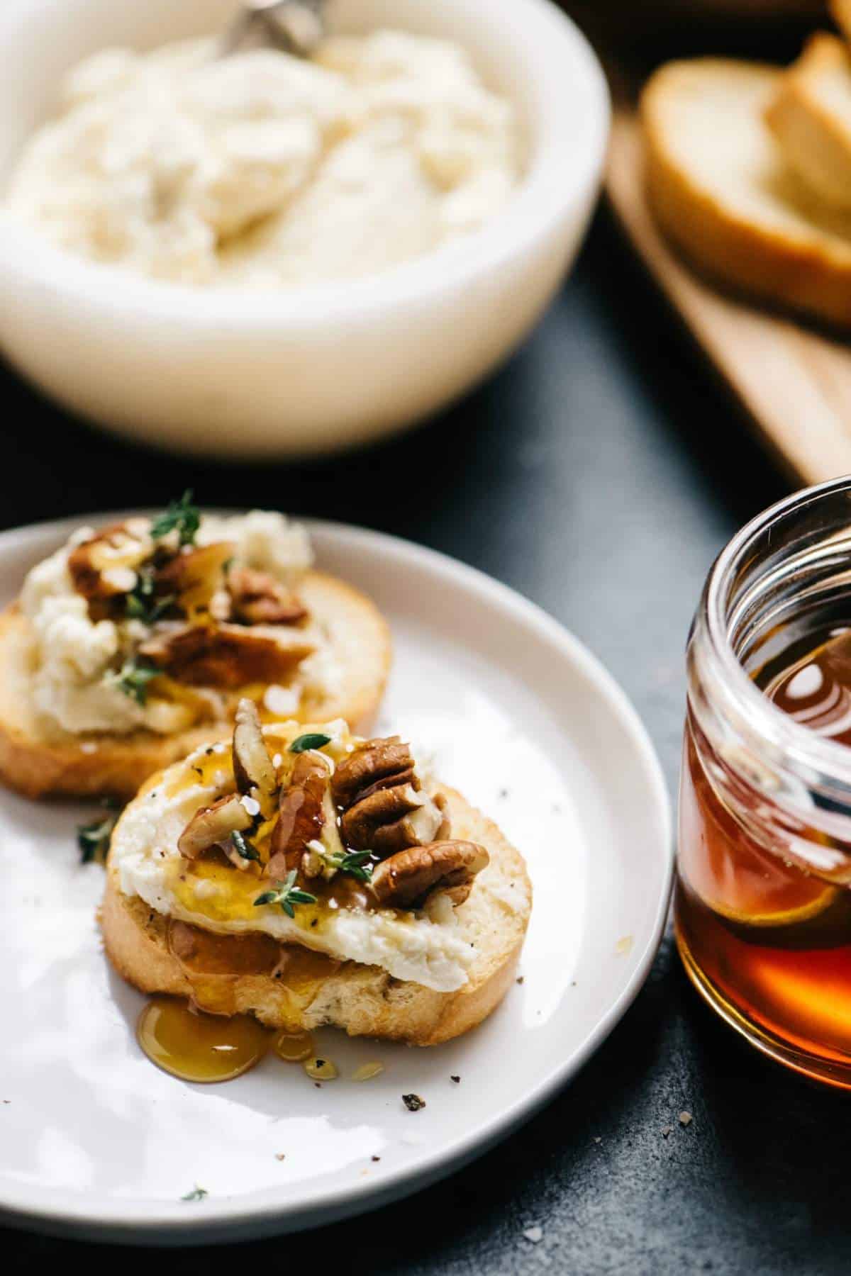 Two goat cheese crostini on a white plate with a honey drizzle.