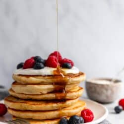 Stack of fluffy yogurt pancakes being drizzled with maple syrup.