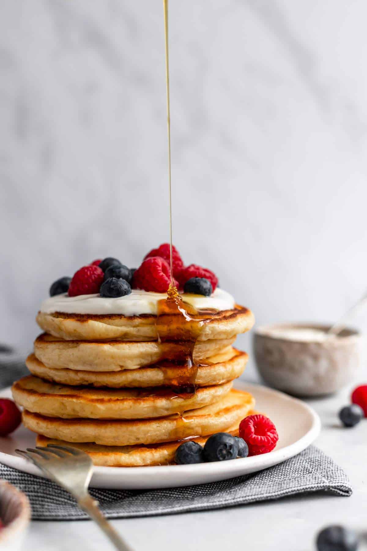 Stack of fluffy yogurt pancakes being drizzled with maple syrup.