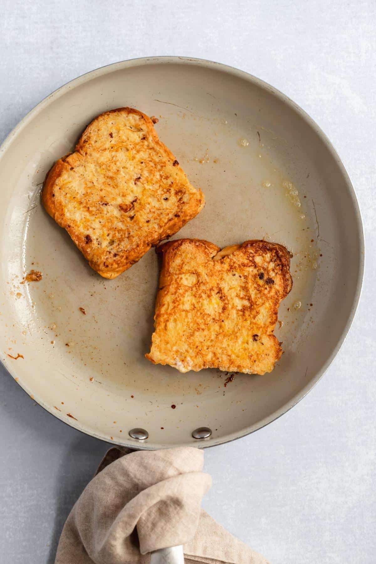 Cooking two pieces of brioche French toast on a large skillet.