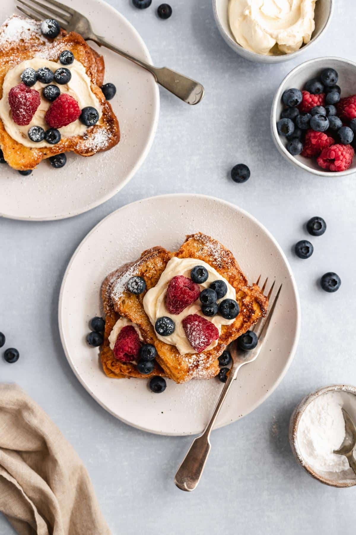 White plates with brioche French toast, whipped cream and berries.