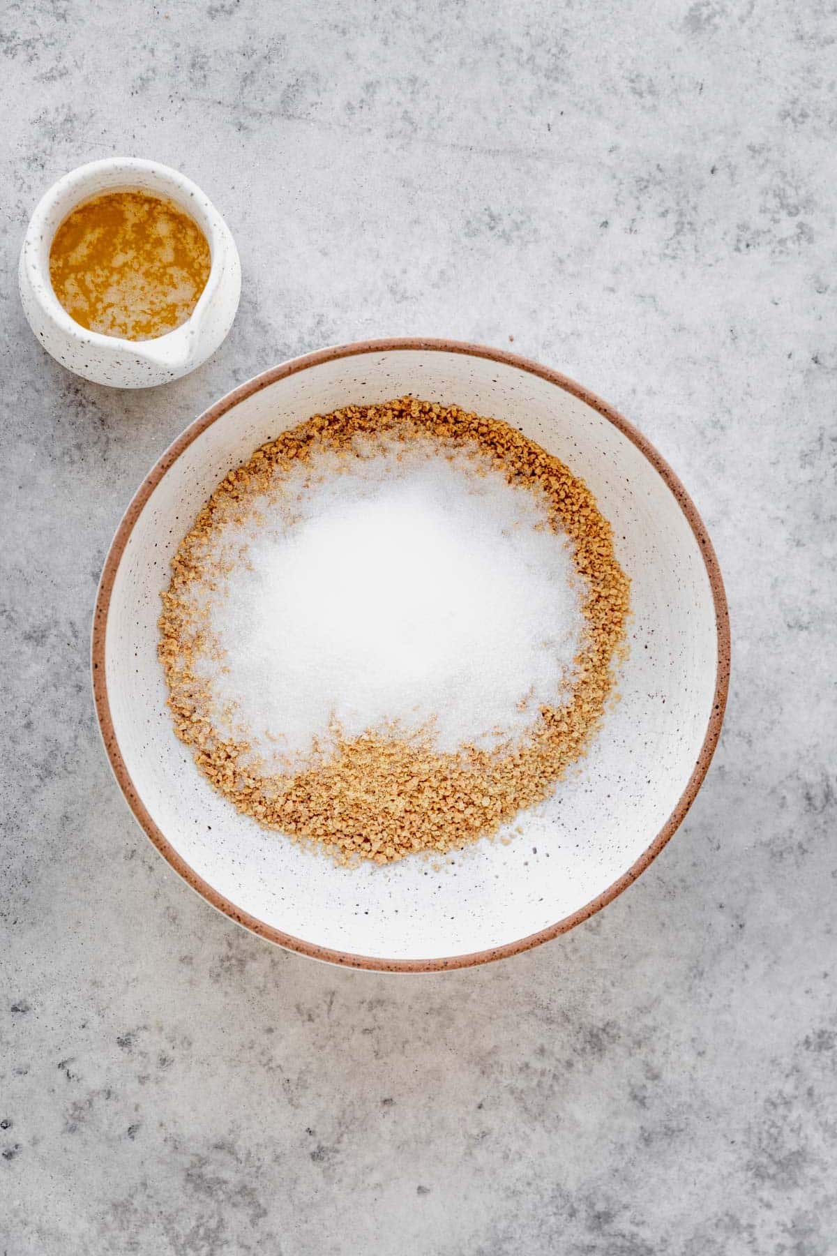 Adding sugar and graham cracker crumbs to a medium bowl.