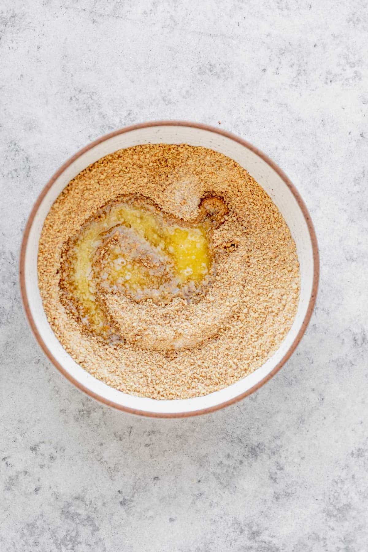 Mixing melted butter into a combination of graham cracker crumbs and sugar.