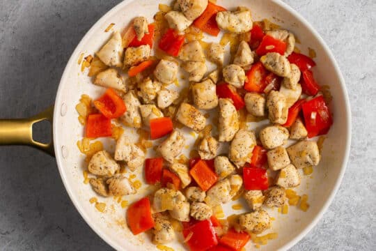 Cooking chicken pieces with sautéed bell pepper and onion.