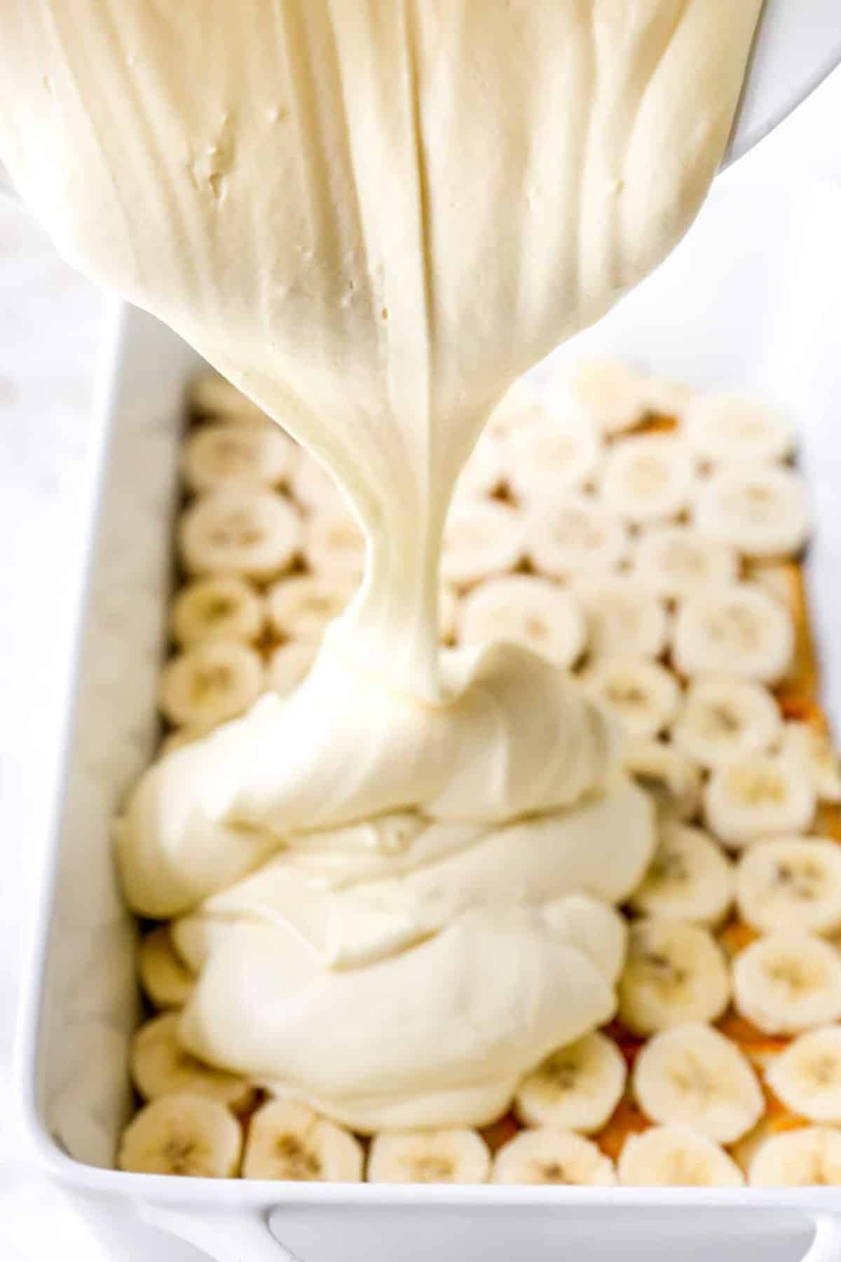 Pouring pudding mixture over cookie and banana layer.