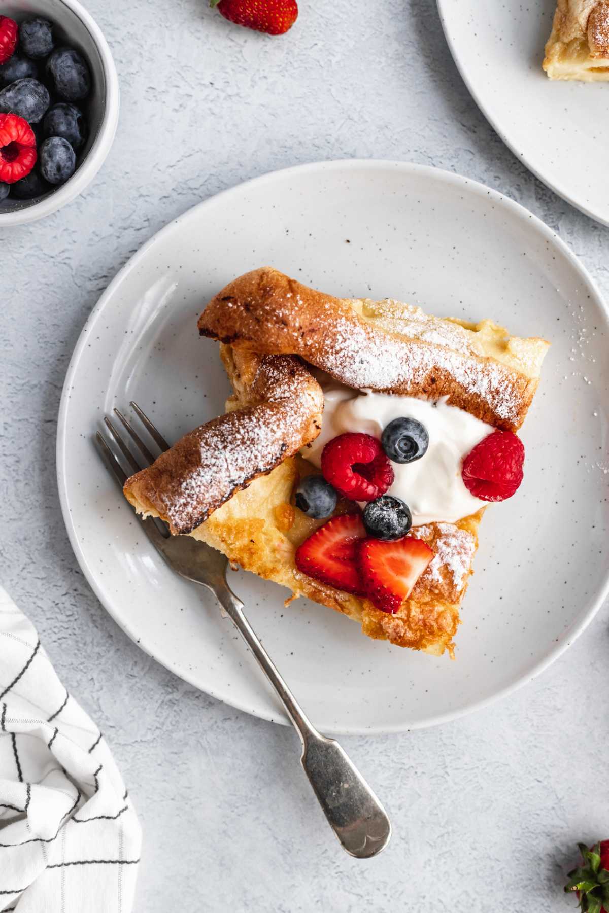 Dutch baby served on a white plate with berries and whipped cream.