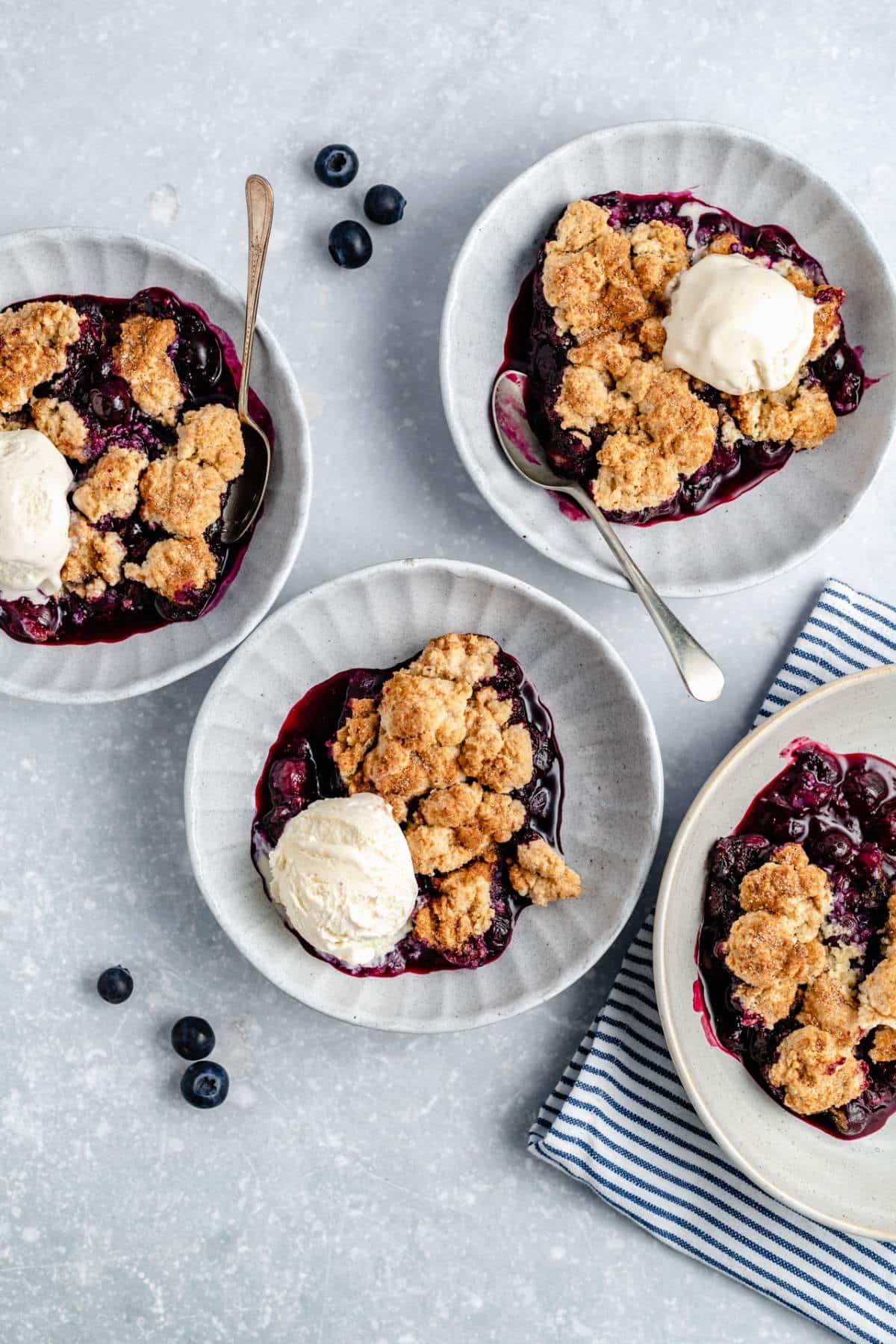 White bowls with blueberry cobbler topped with ice cream.