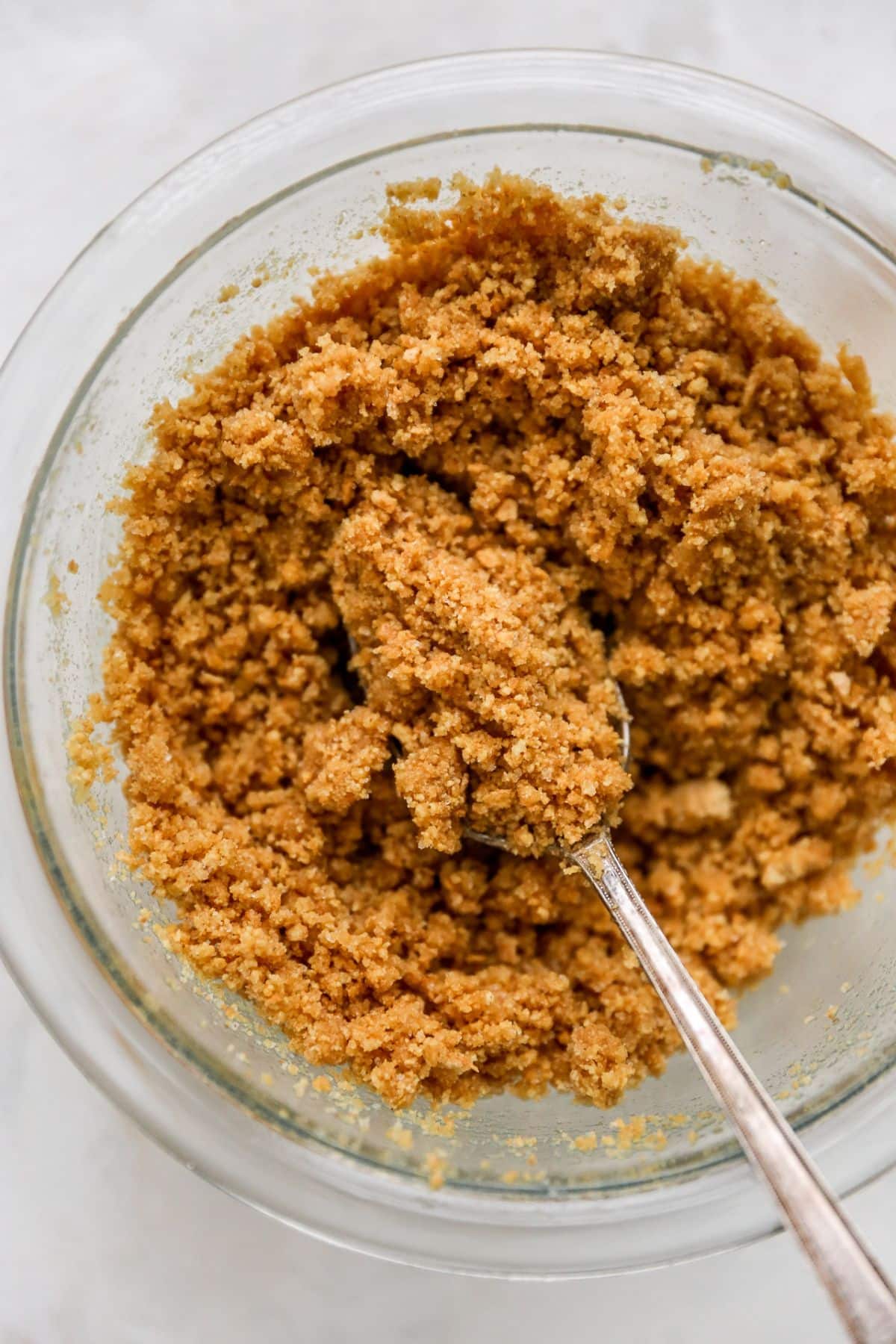 Mixing graham cracker crumbs with melted butter in a bowl.