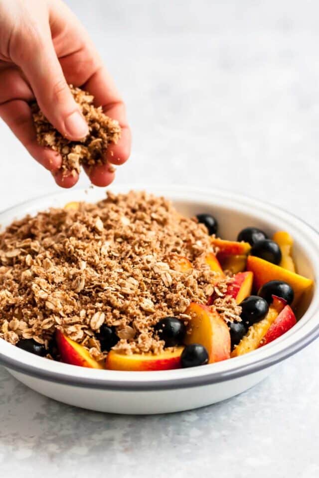 Hand adding crisp topping to fruit dessert in a pie plate.