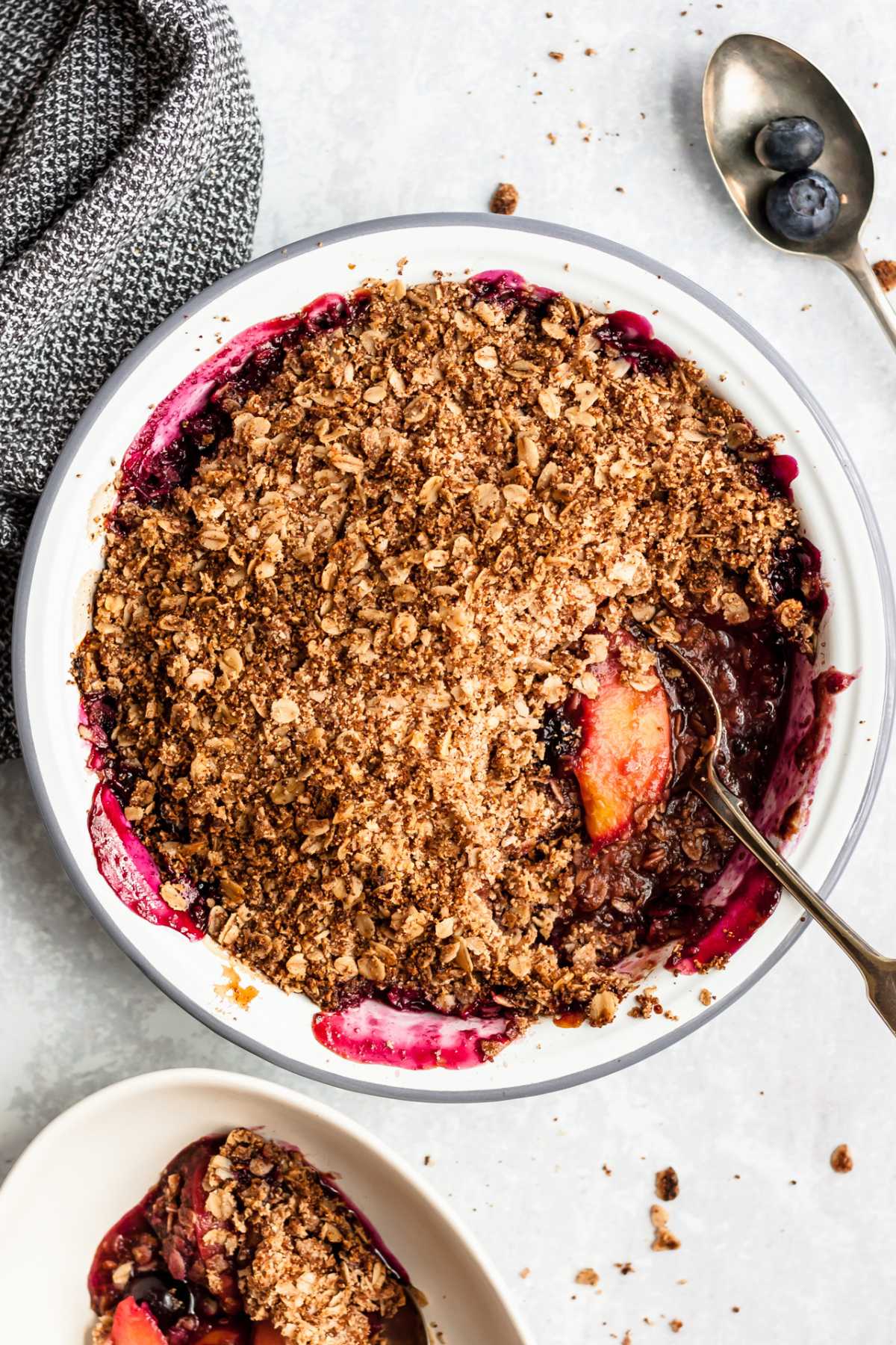 Peach Blueberry Crisp in a white pie plate with a serving spoon.