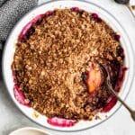 Peach Blueberry Crisp in a white pie plate with a serving spoon.