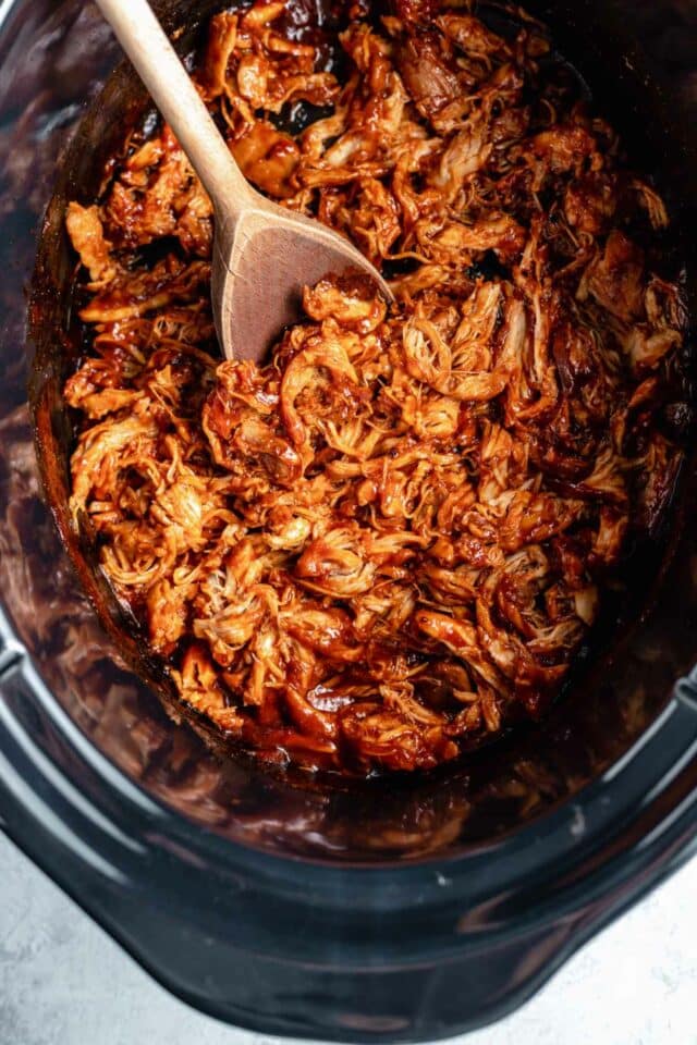 Using a wooden spoon to stir shredded chicken in a slow cooker.