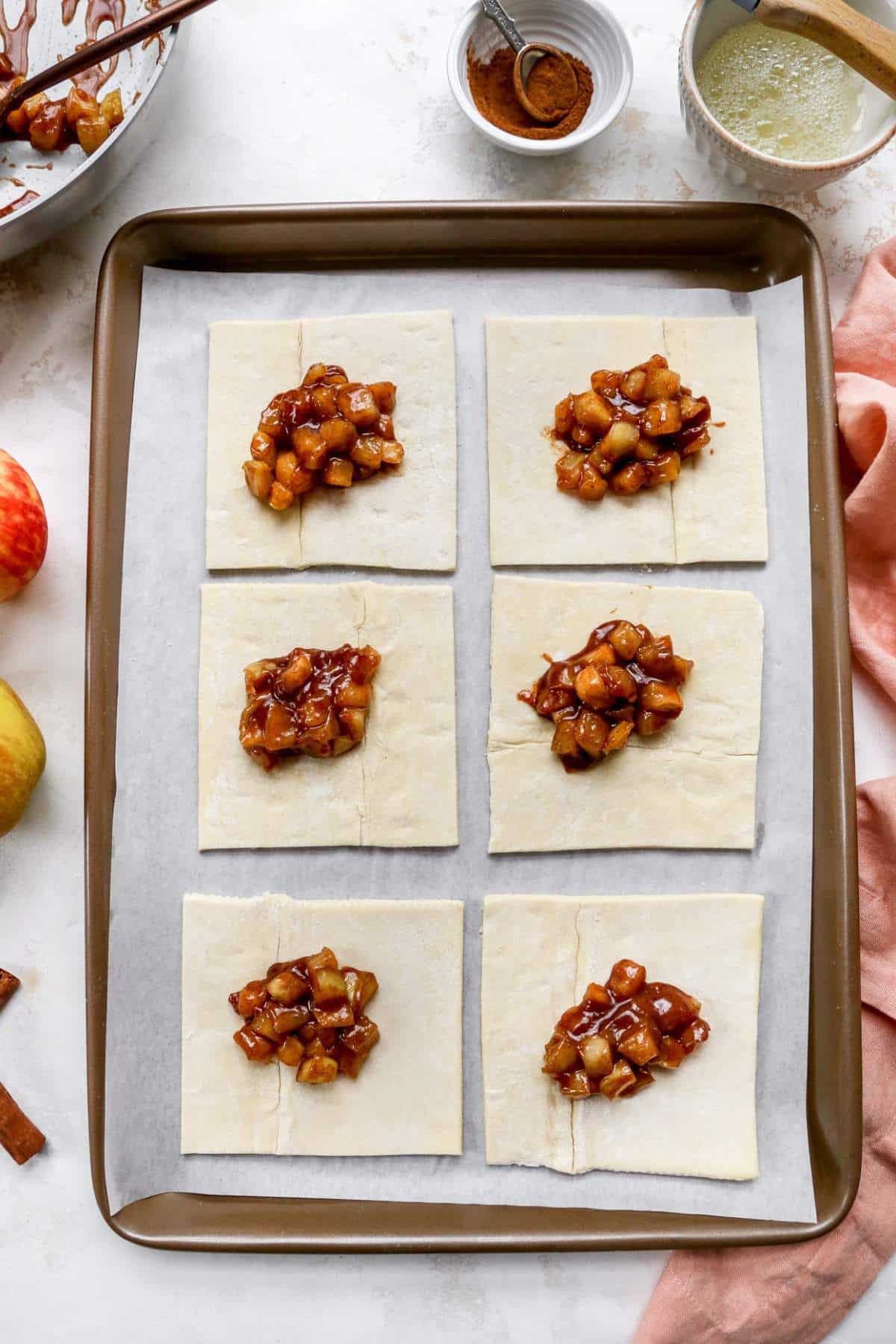 Apple pie filling in the center of puff pastry squares on a baking pan.