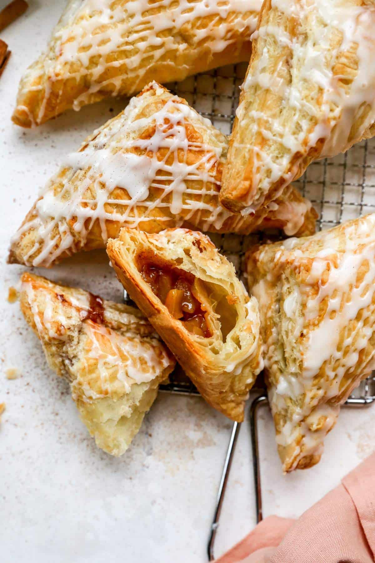 Apple turnovers drizzled with icing with one cut open.