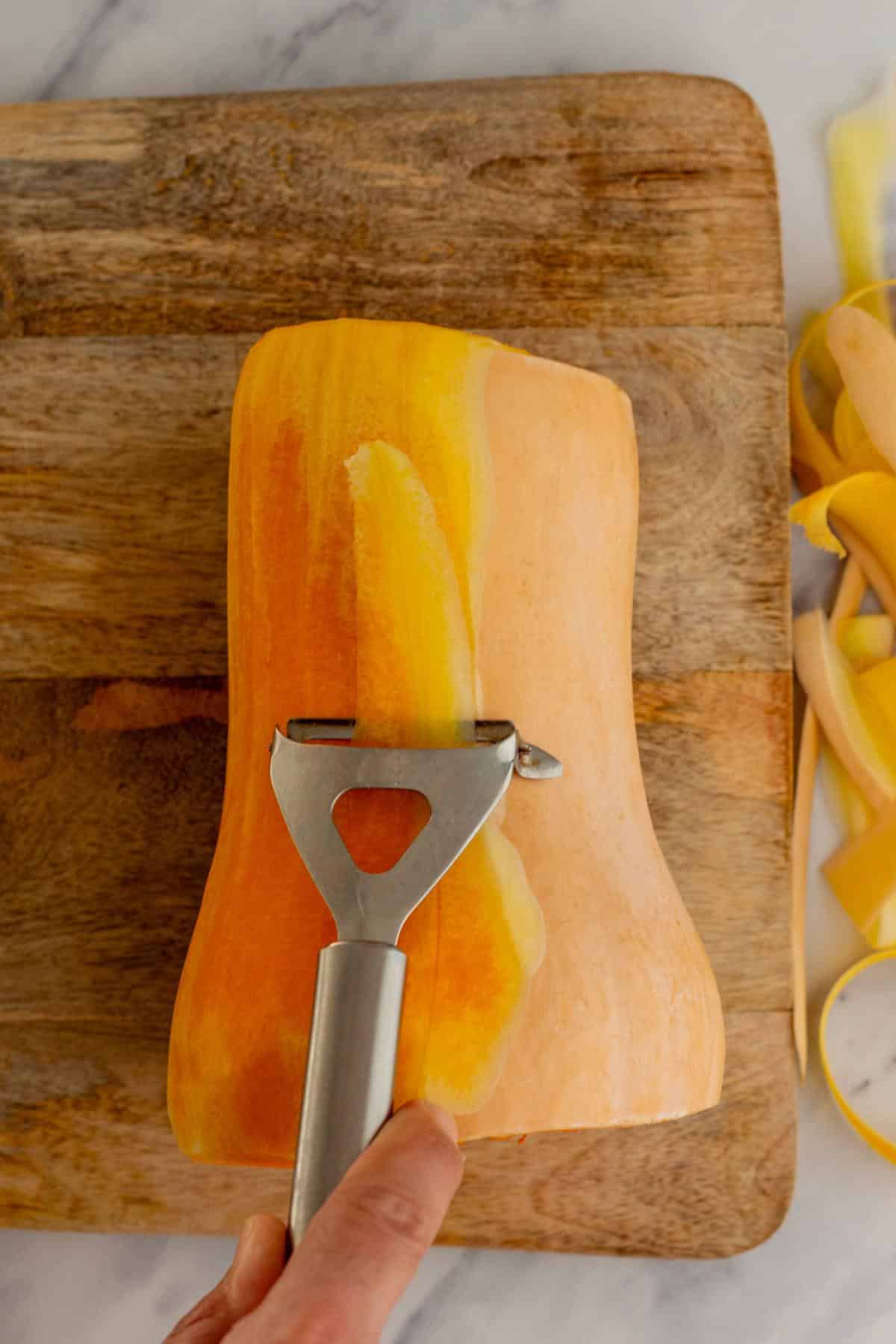 Peeling a butternut squash on a cutting board.