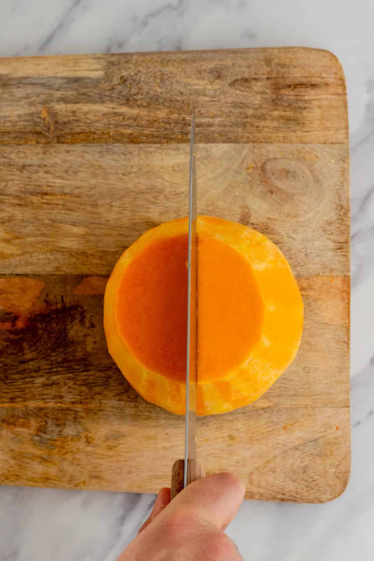 Slicing a butternut squash in half on a cutting board.