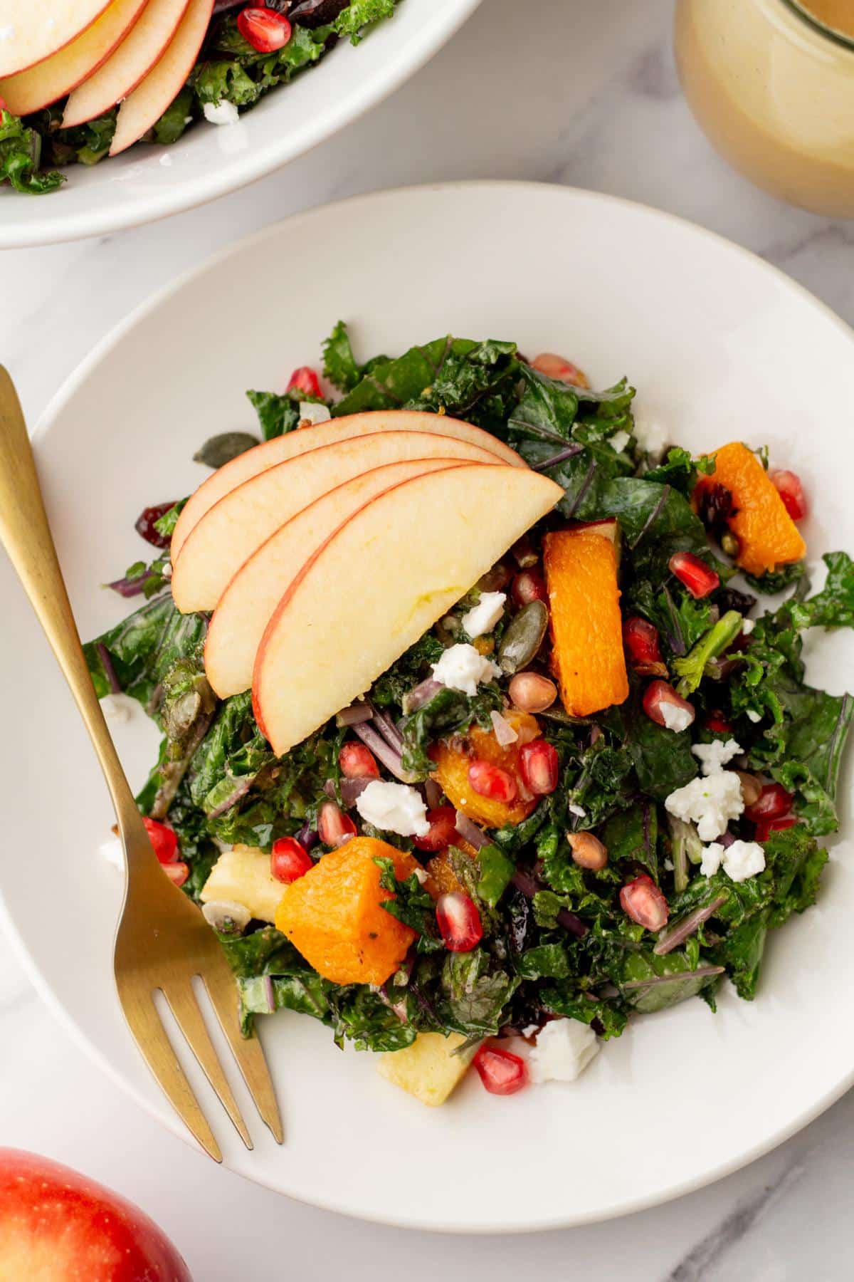 Butternut squash salad topped with a sliced apple on a white plate.