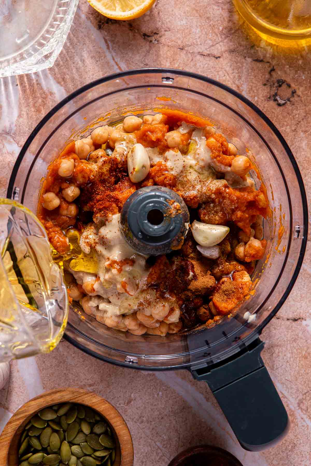 Pouring olive oil into a food processor with chickpeas, spices and pumpkin puree.