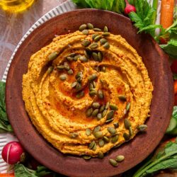 Pumpkin hummus in a bowl surrounded by raw veggies.