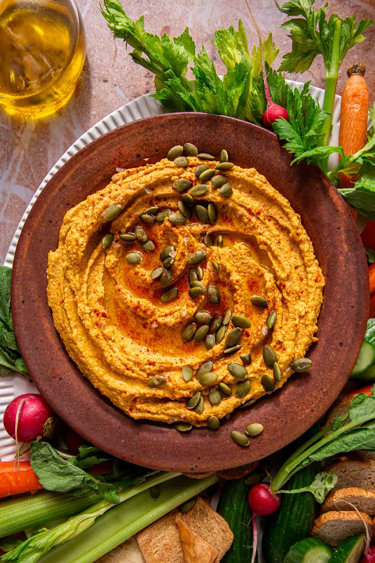 Pumpkin hummus in a bowl surrounded by raw veggies.