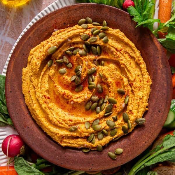 Pumpkin hummus in a bowl surrounded by raw veggies.