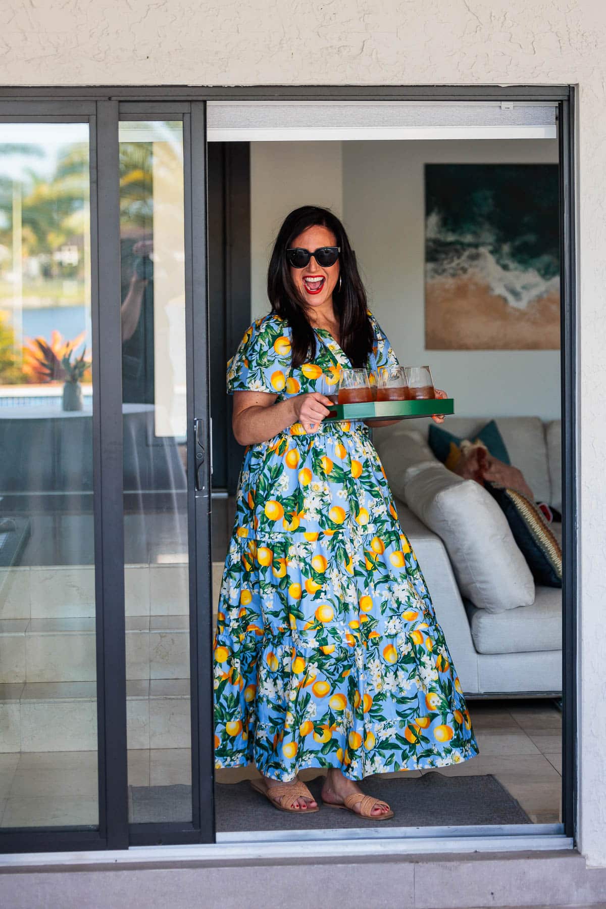 Woman bringing a tray filled with drinks out a door.