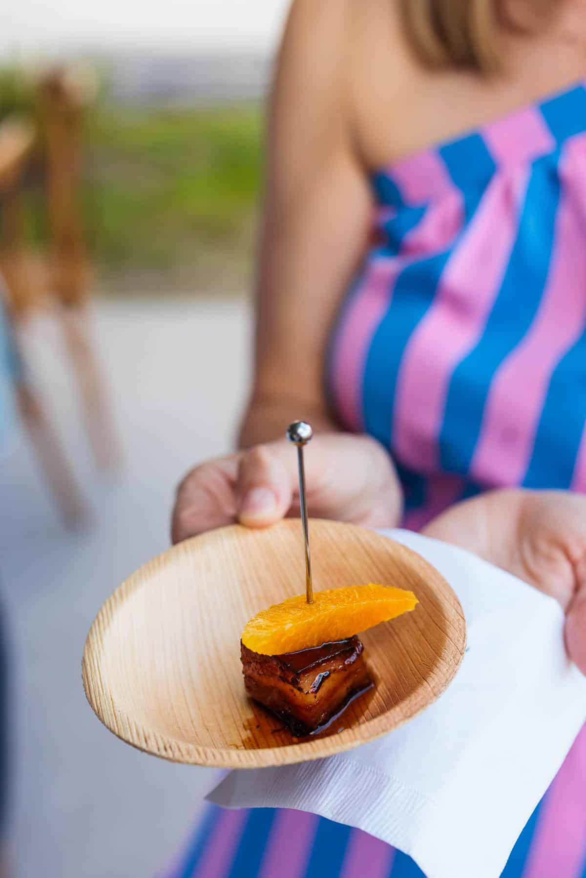 Pork belly appetizer with an orange slice in a small bowl.