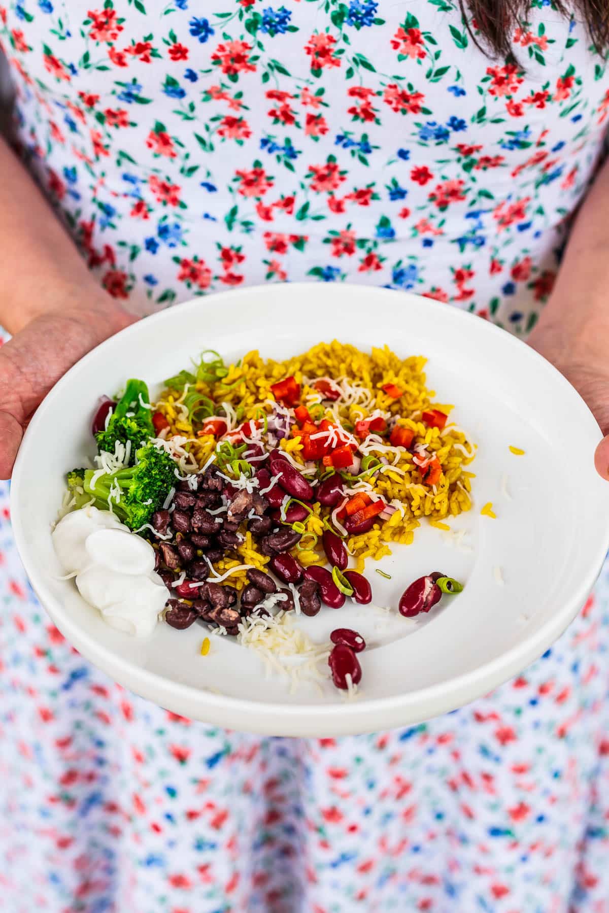 Holding a white bowl filled with rice, beans and veggies.