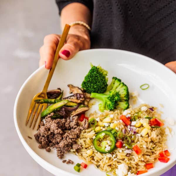 Woman holding a bowl with rice, broccoli and ground turkey.