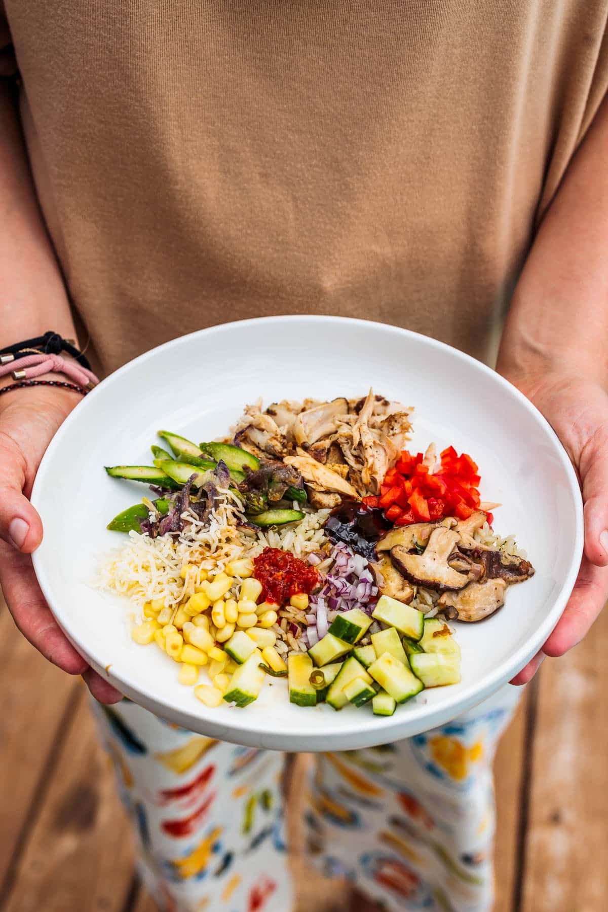 Woman holding a rice bowl made with shredded chicken and vegetables.