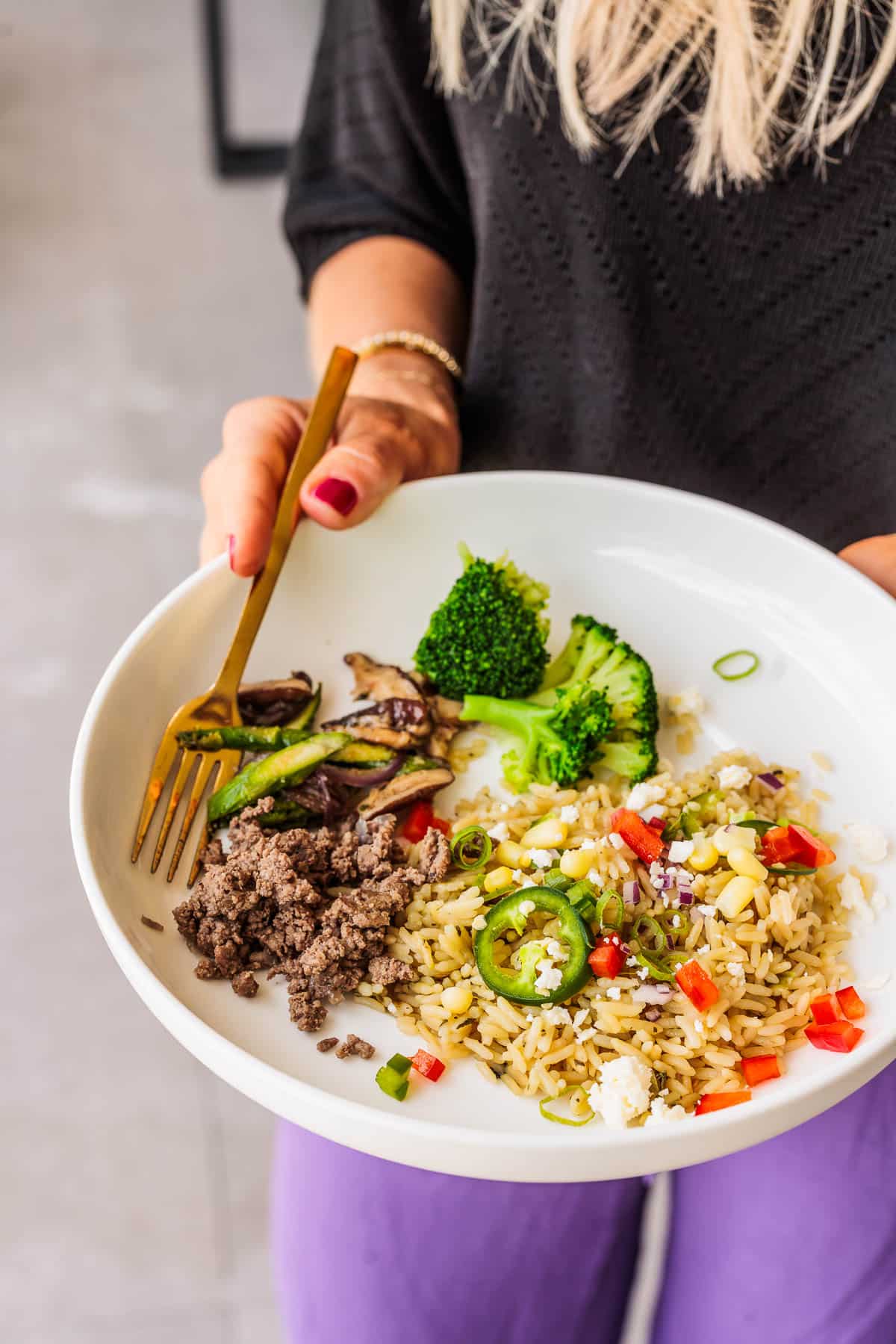 Woman holding a bowl with rice, broccoli and ground turkey.