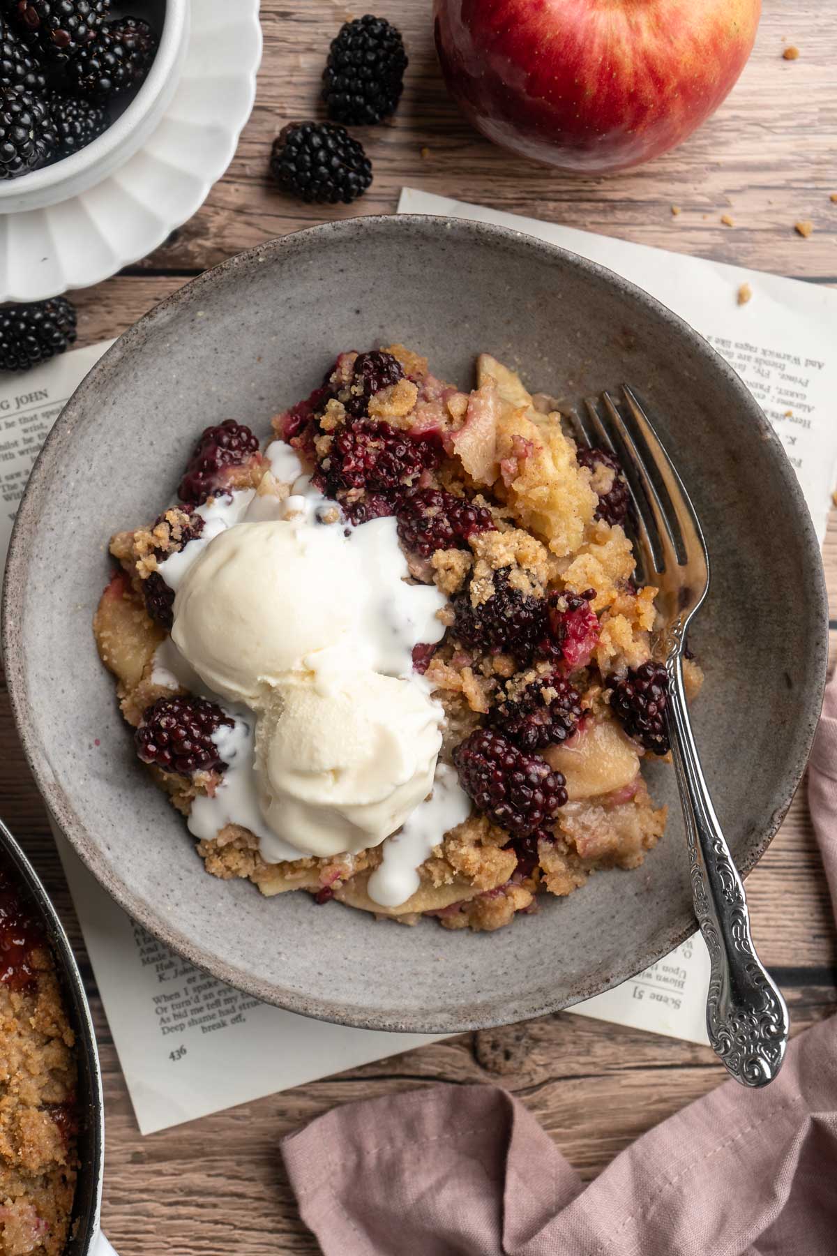 Apple blackberry crumble topped with two scoops of vanilla ice cream.