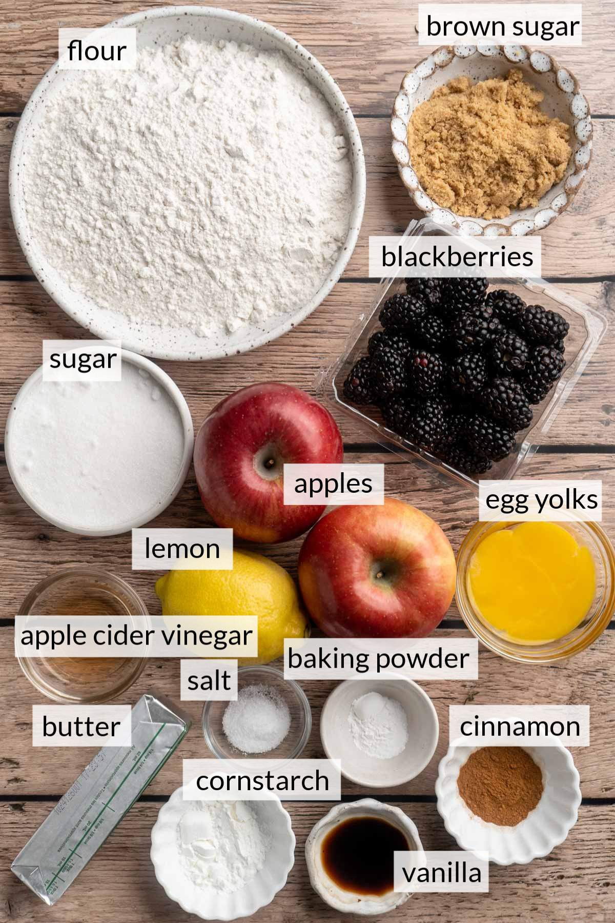 Blackberries and apples near bowls of flour, sugar, egg yolk and cinnamon.